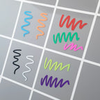 Prov på hur de åtta färgerna (plus svart) från setet med 8 kritpennor i klara färger ser ut mot grå bakgrund.